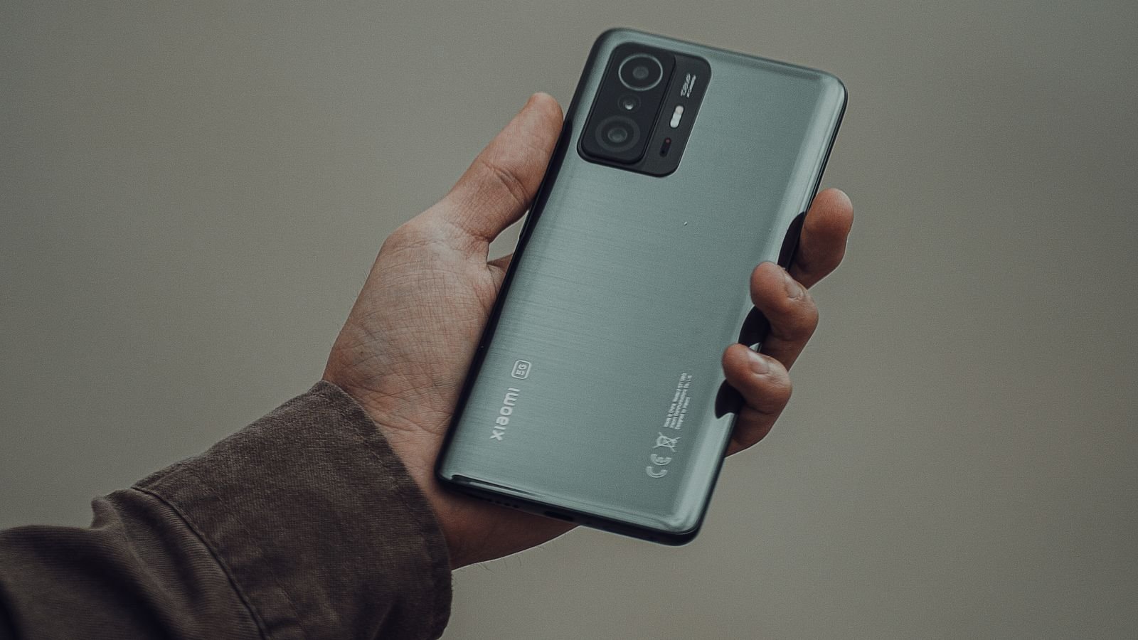 A close-up shot of a hand holding a modern smartphone against a grey background, representing the global foldable smartphone shipment surge