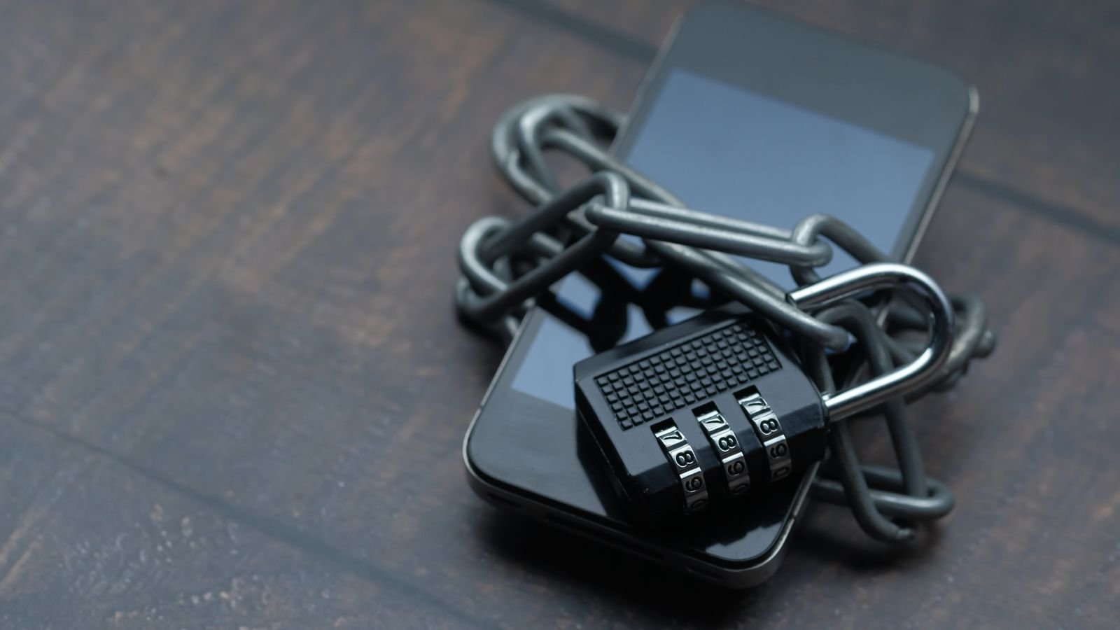 Close-up of a smartphone wrapped in a metal chain with a padlock, symbolizing device security and privacy protection